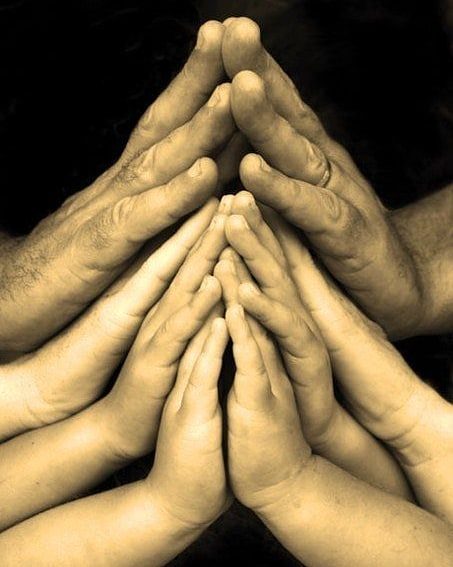 Mani di adulti e bambini unite a formare un triangolo, simbolo di fratellanza